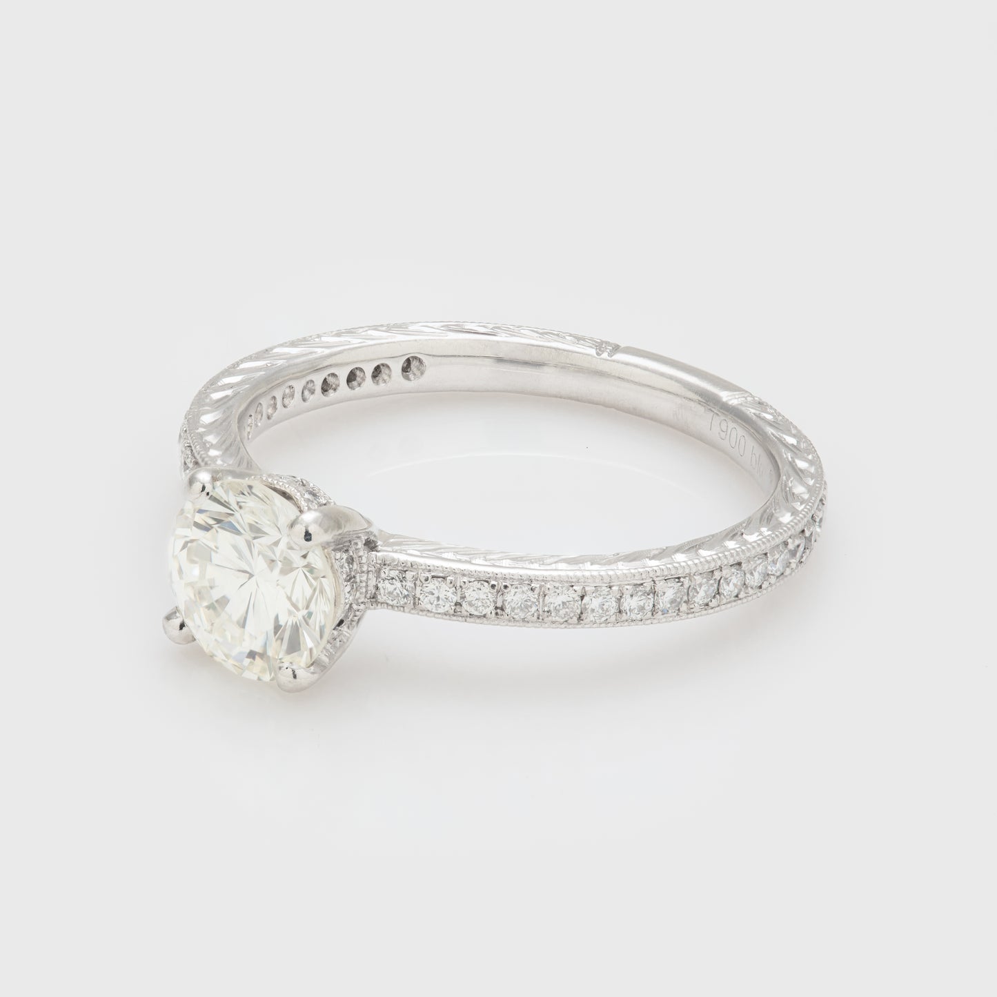 Side view of a platinum ring with a diamond and diamonds on the gallery and along the shank accented by engraving and milgraining.