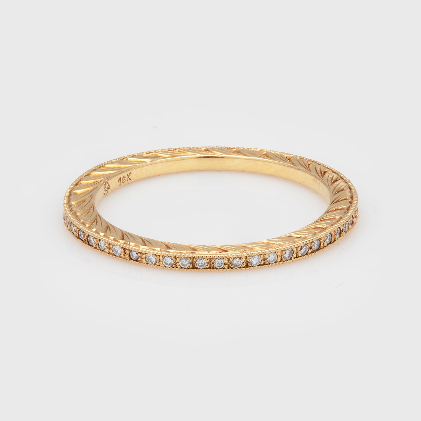 Close-up of an 18k yellow gold band with diamonds and milgrain edge accents.