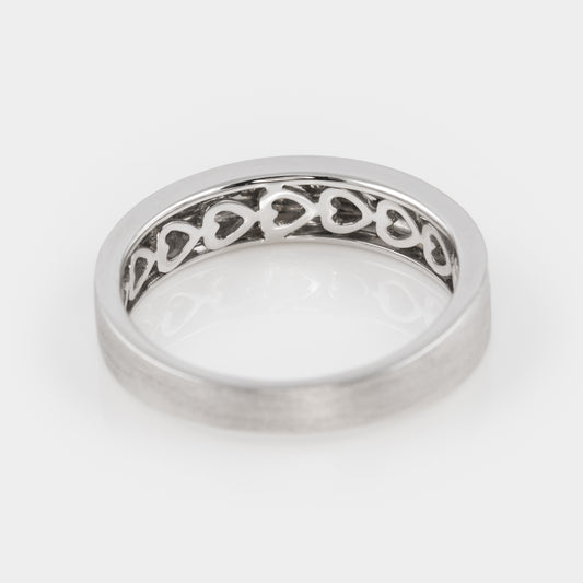 Silver ring with heart motif on the inner band, on a white background