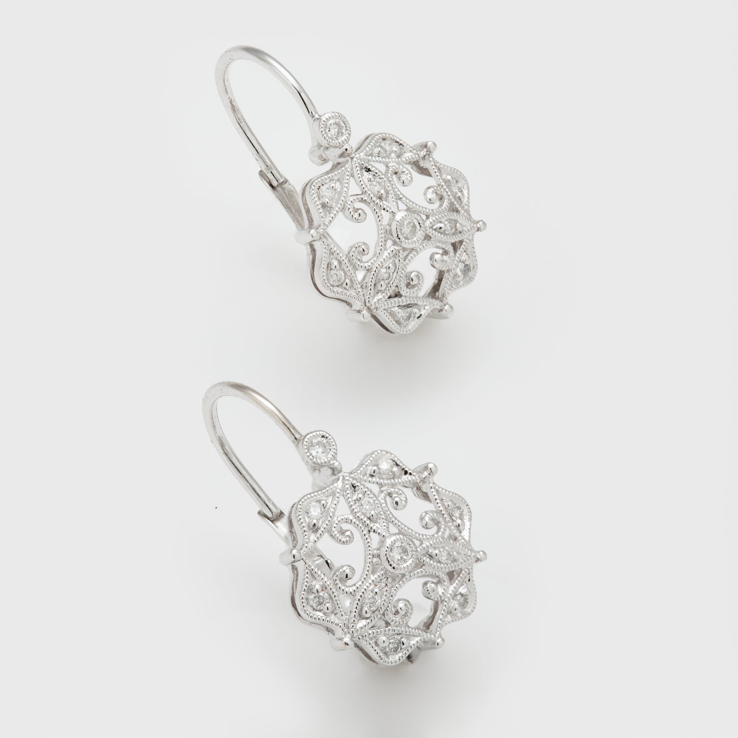 Close-up of 14k white gold earrings with round brilliant cut diamonds and milgrain details.