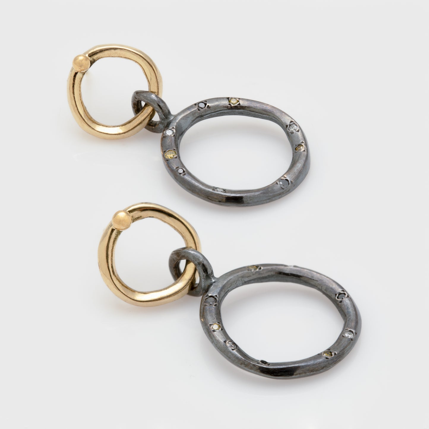 Close-up of earrings in 18k yellow gold and oxidized sterling silver with yellow, white, and black diamonds.