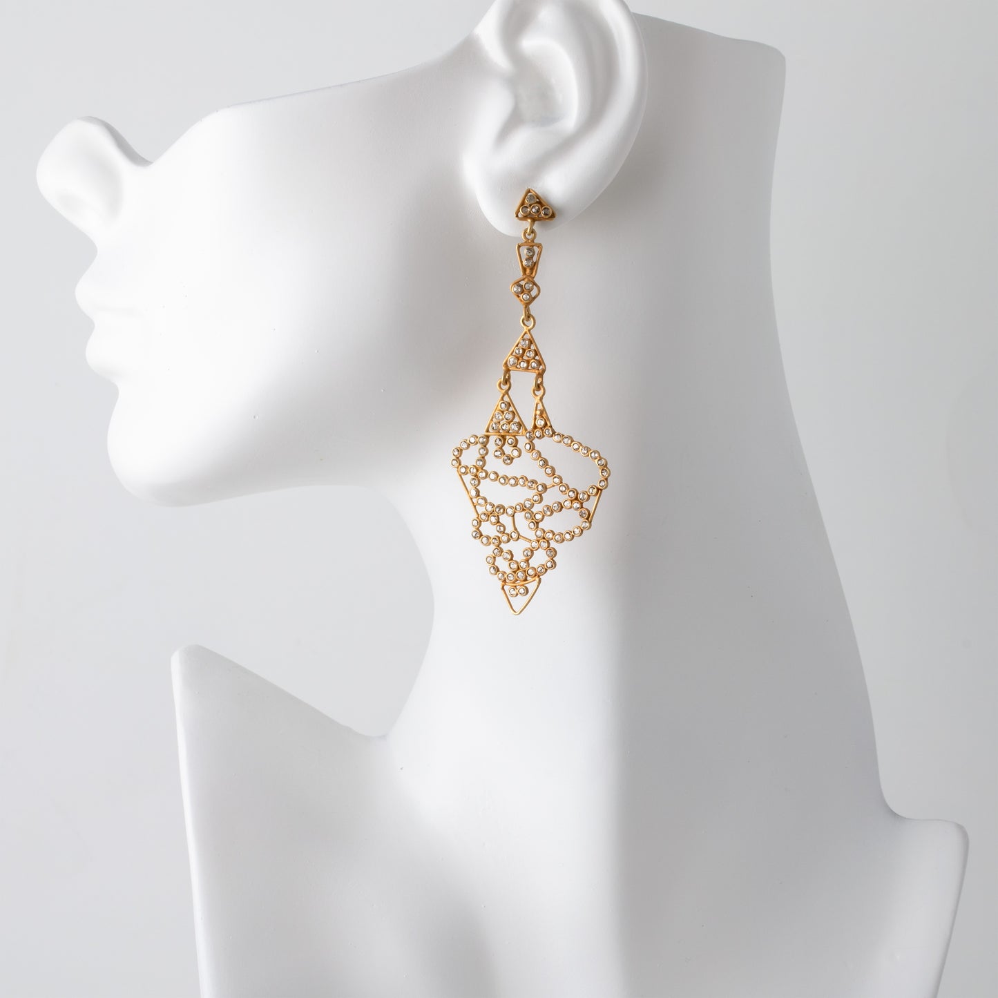 Gold earrings on a mannequin ear with a plain background