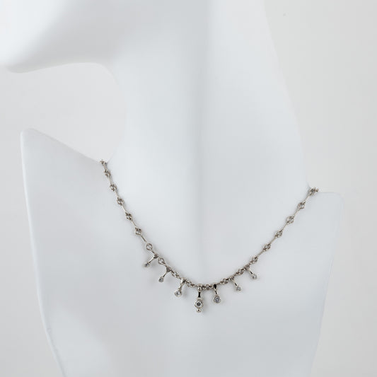 A silver-toned necklace displayed on a white mannequin bust against a white background.