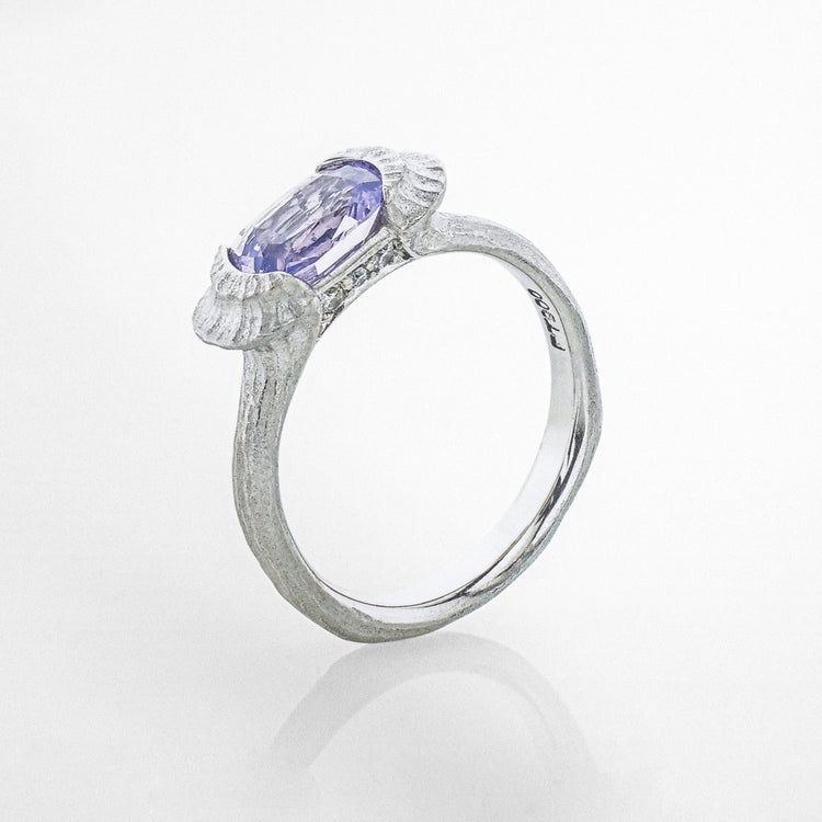 Close-up of a platinum ring with an organic texture, set with a light purple sapphire and accented by pave set diamonds.
