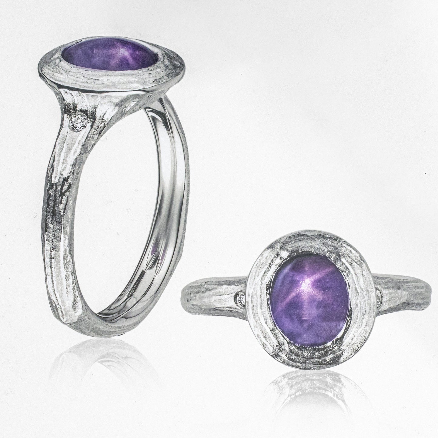 A platinum ring with a central purple star sapphire gemstone, surrounded by a textured design, and a smaller, matching purple star sapphire as a pendant.