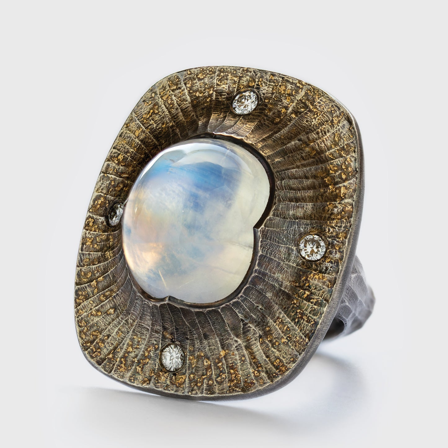 Close-up of an Argentium silver ring with a rainbow moonstone and diamond accents, featuring 22k gold dust.