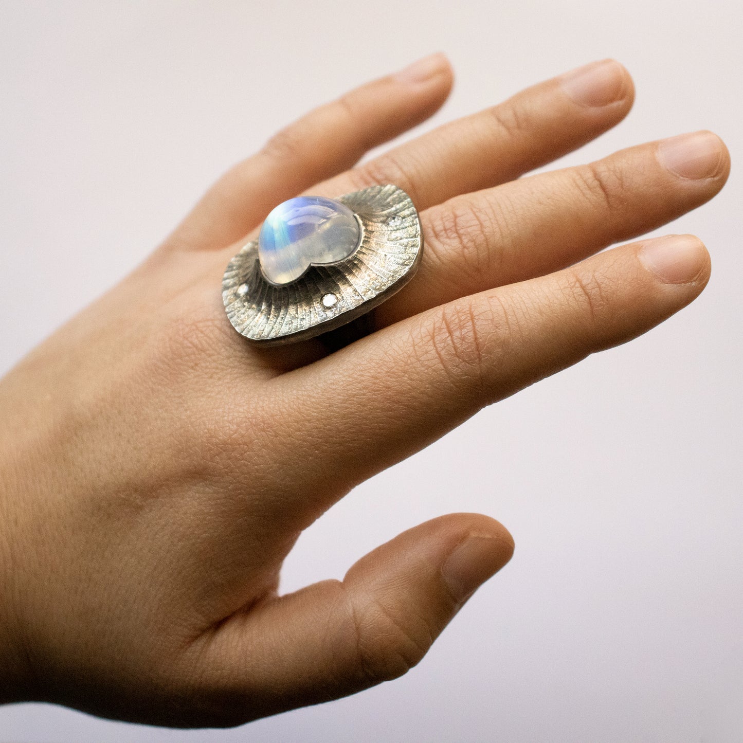 Worn on hand, an Argentium silver ring with rainbow moonstone and four accent diamonds. Features 22k gold dust and a hidden interior diamond.