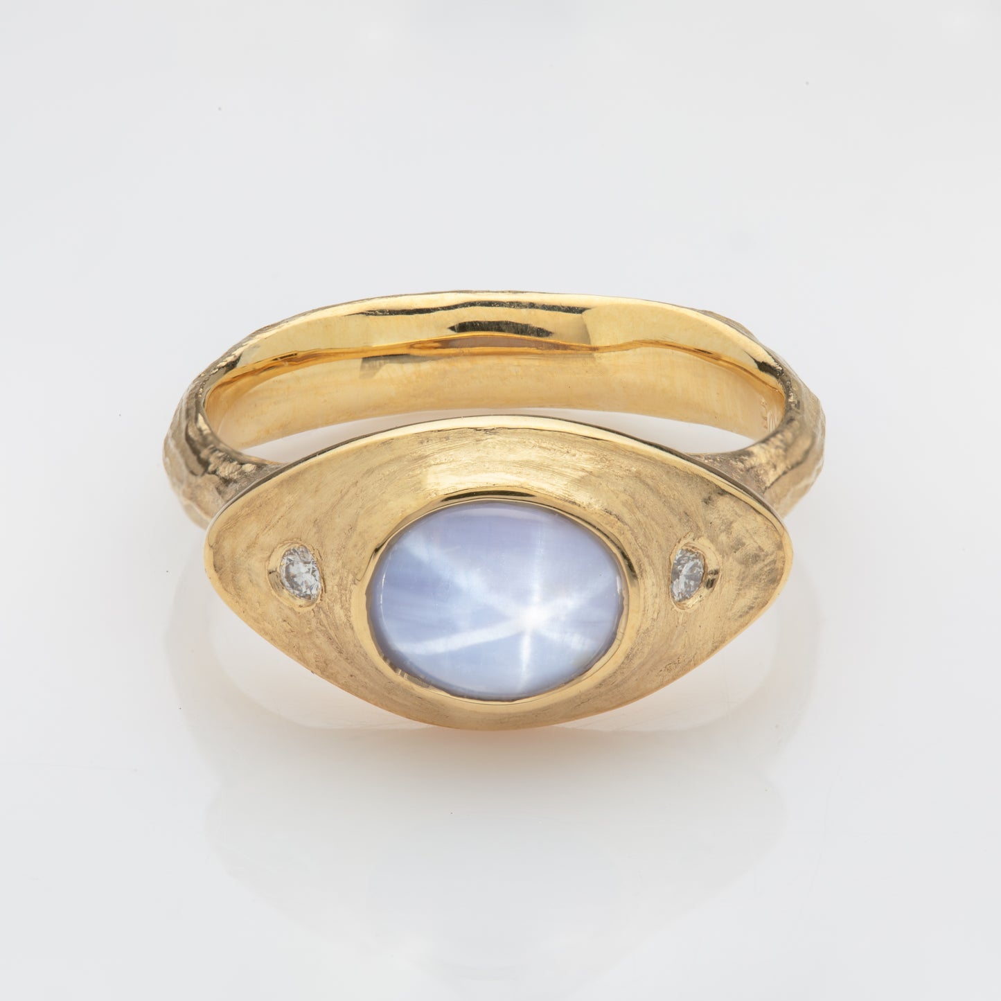 Close-up of an 18k yellow royal gold ring with a pale gray-blue Star Sapphire and diamond accents.