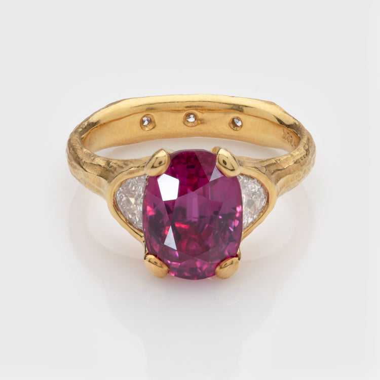 Close-up of a 22k yellow gold ring featuring a ruby with diamond accents and a redwood bark texture.