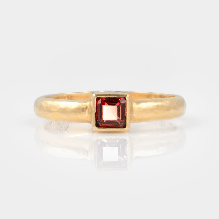Front view of an 18k yellow gold ring, satin finish hammered band, with a square step cut garnet.
