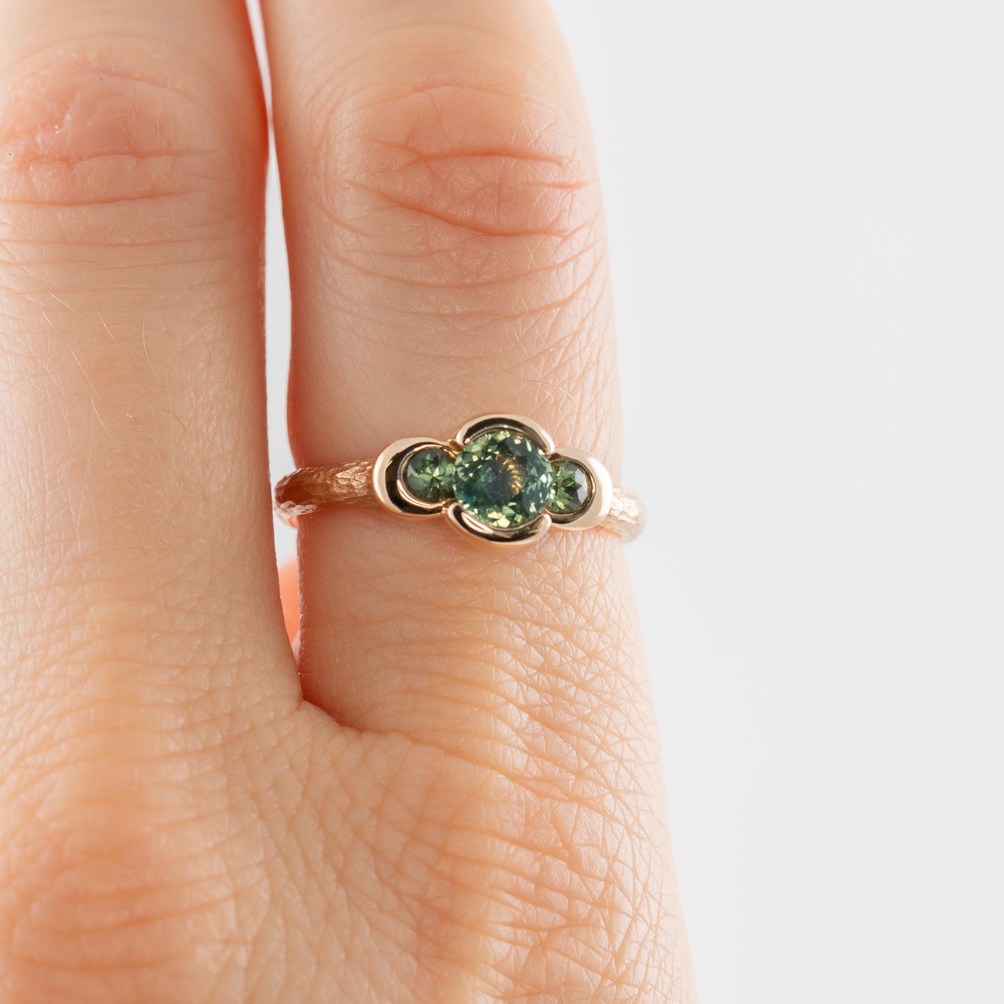 Gold ring with green gemstones on a finger against a light background
