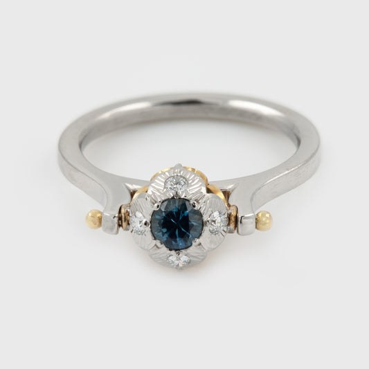 Platinum two-tone ring featuring a round blue sapphire center stone surrounded by small diamonds, with a polished silver-colored band and gold accents. Photographed on a white background.