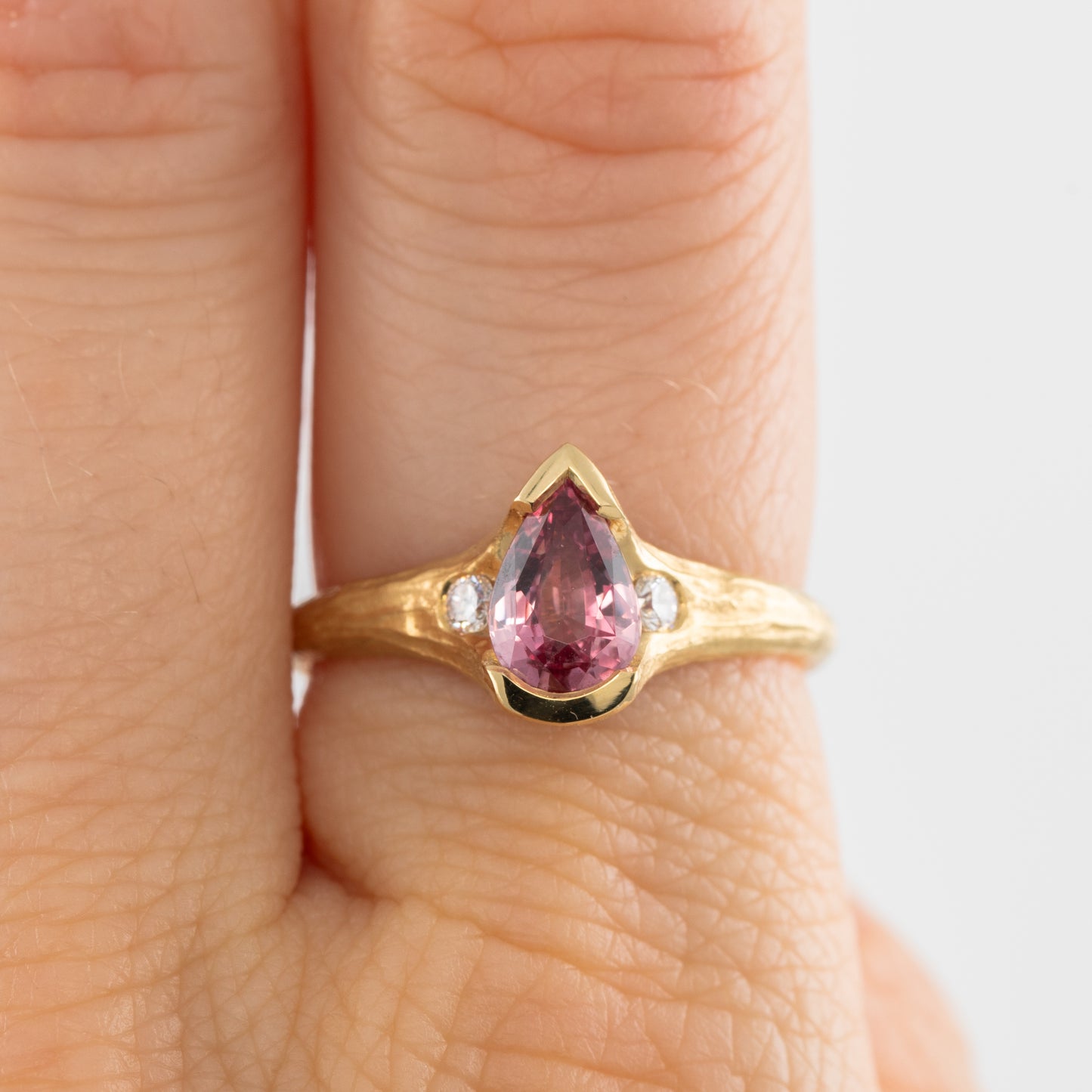 Gold ring with a pink gemstone on a finger against a white background