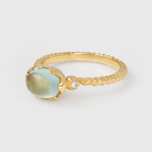 Gold ring with a green and blue gemstone and diamond on a light gray background