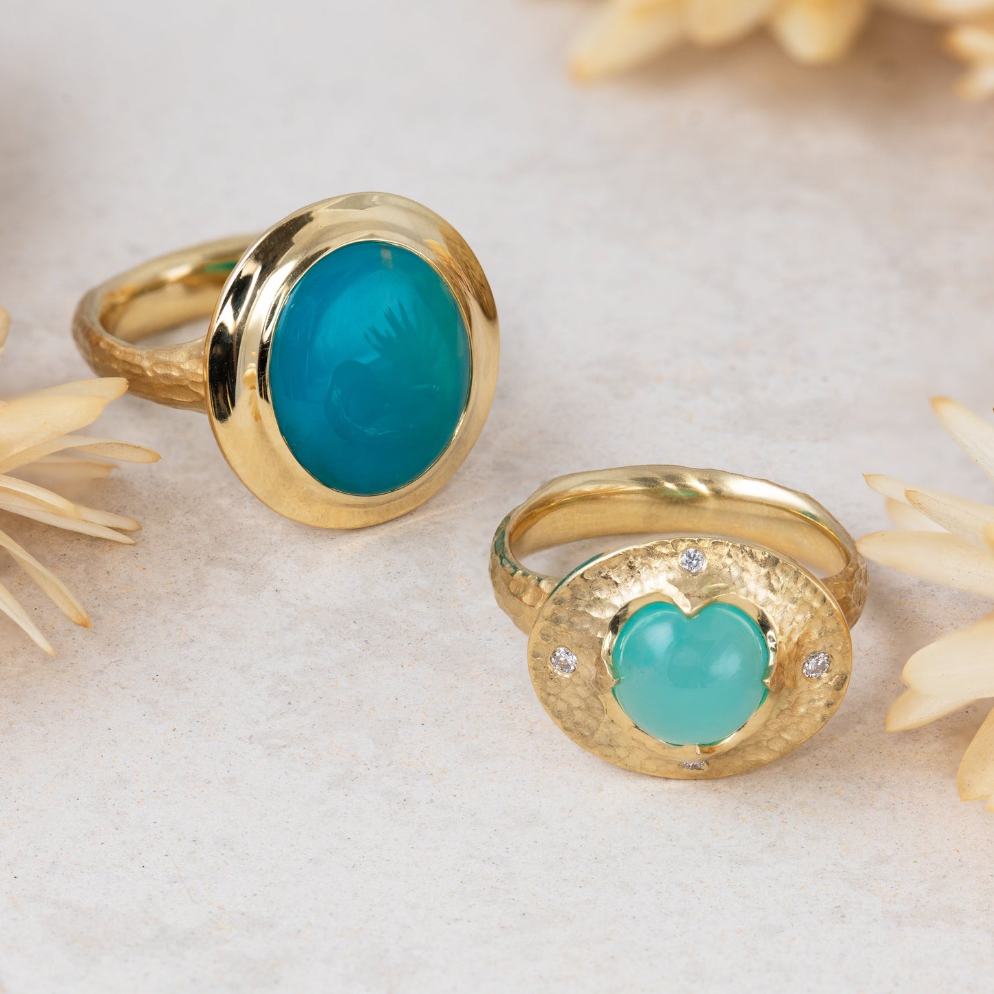 Gold rings with blue stones on a light surface with dried flowers.