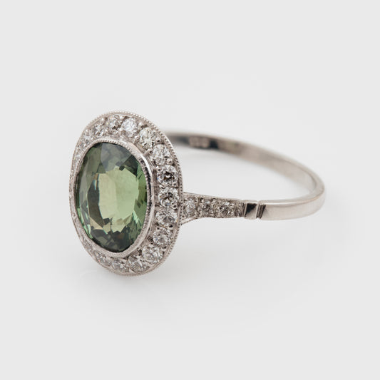 Platinum ring with a green Alexandrite gemstone and diamond accents on a white background