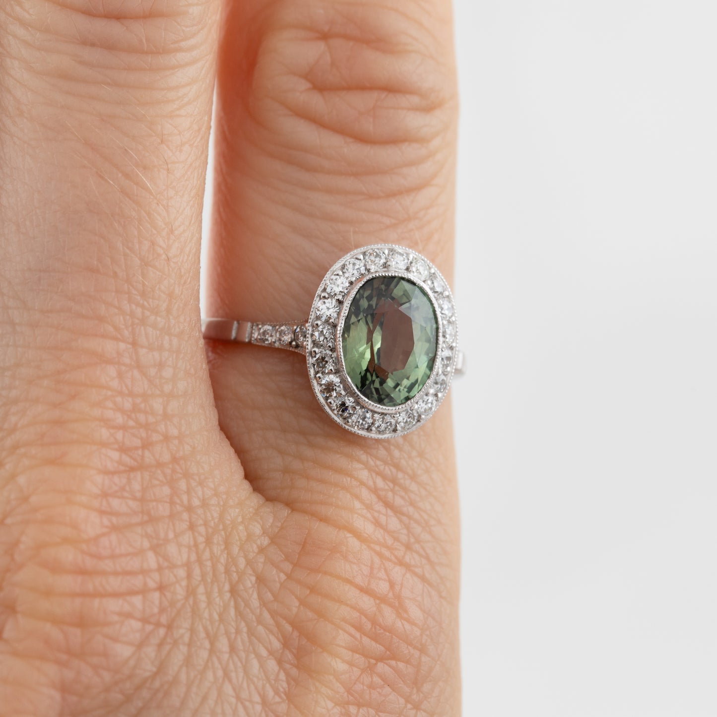 Ring with a green Alexandrite gemstone on a finger against a white background