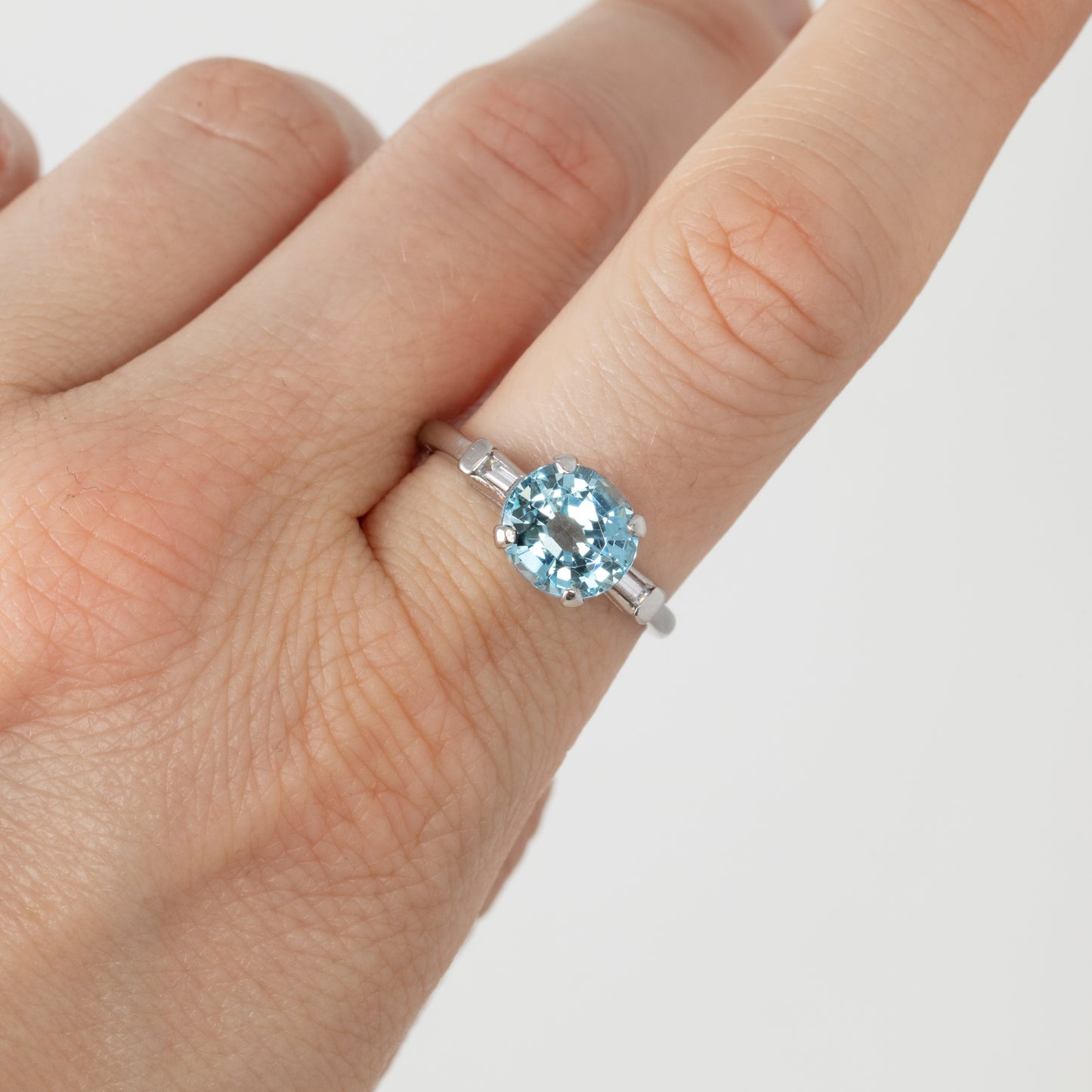 Hand wearing a ring with a blue gemstone on a plain background
