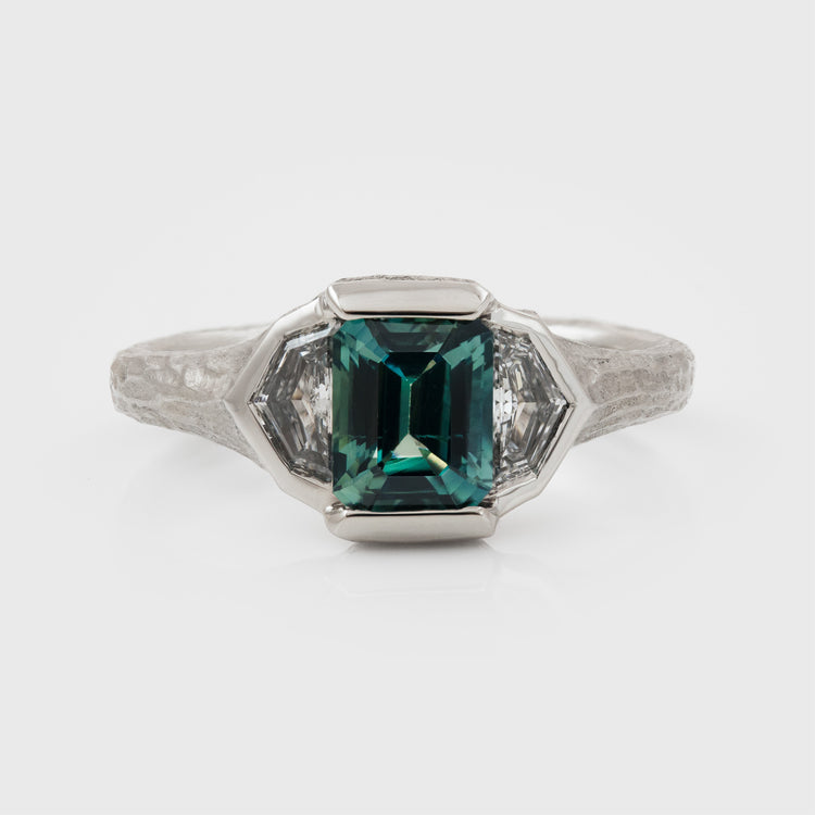 Platinum ring with green center gemstone and two accent diamonds on a white background