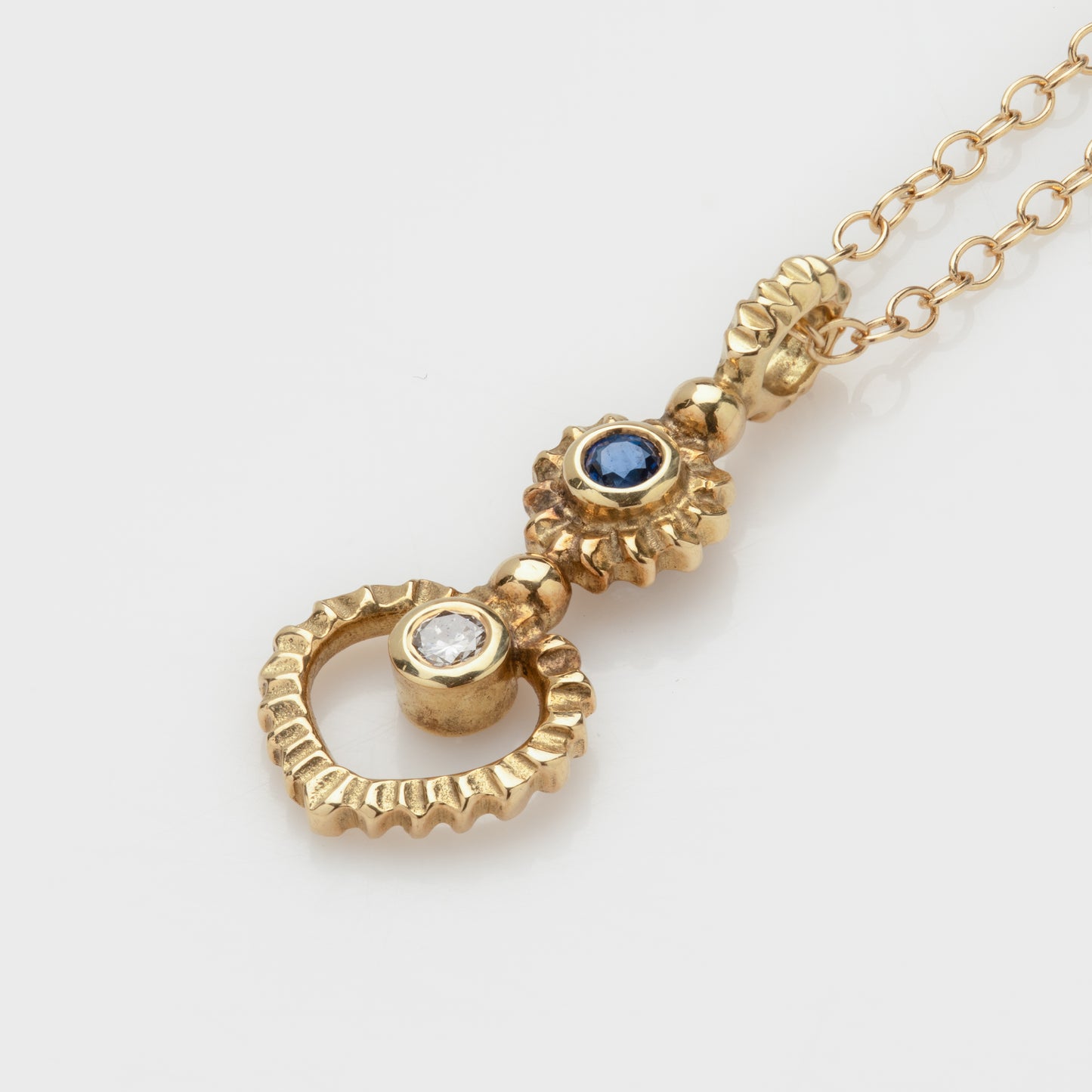 Close-up of an 18k yellow gold necklace with a diamond and sapphire.