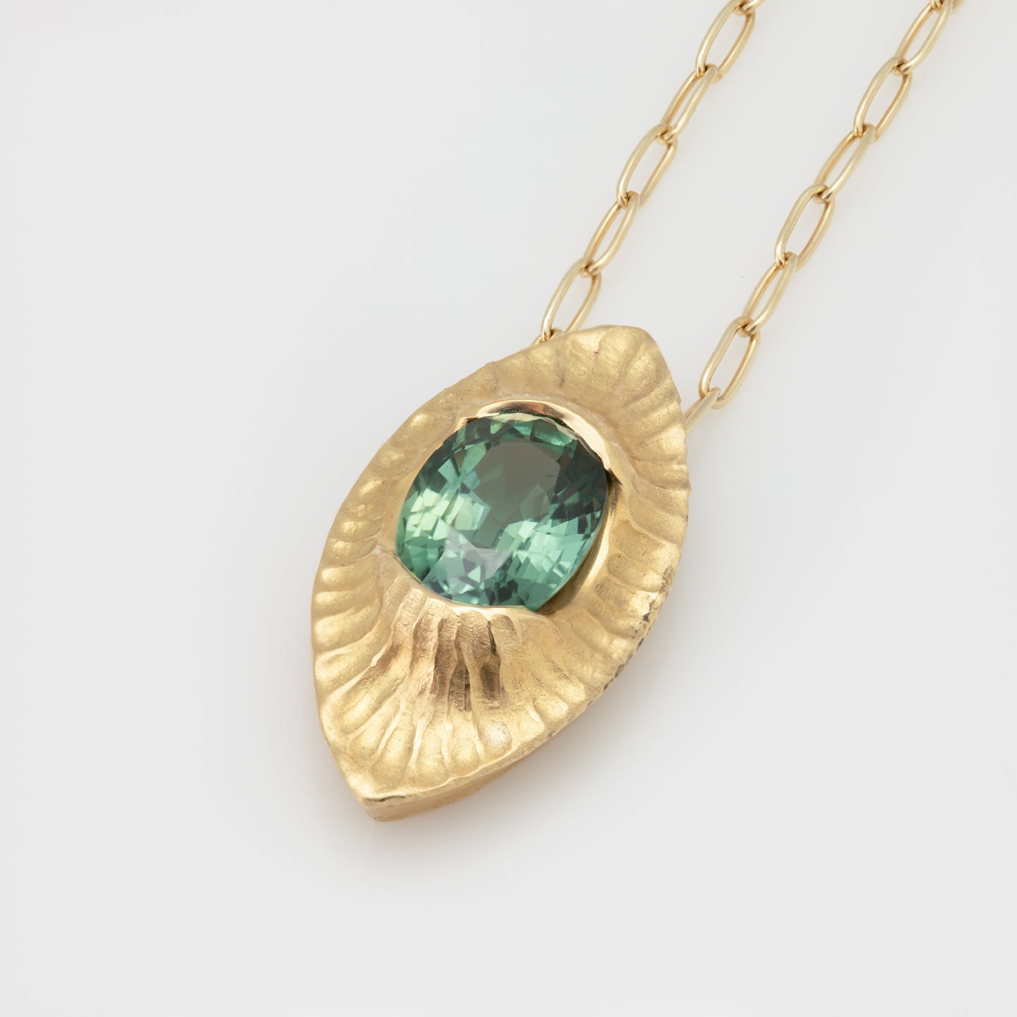 Close-up of an 18k yellow gold necklace with a faceted oval green sapphire.
