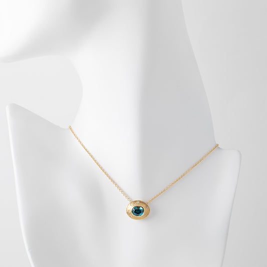 Gold necklace with a blue zircon gemstone and small accent diamonds on a white mannequin background