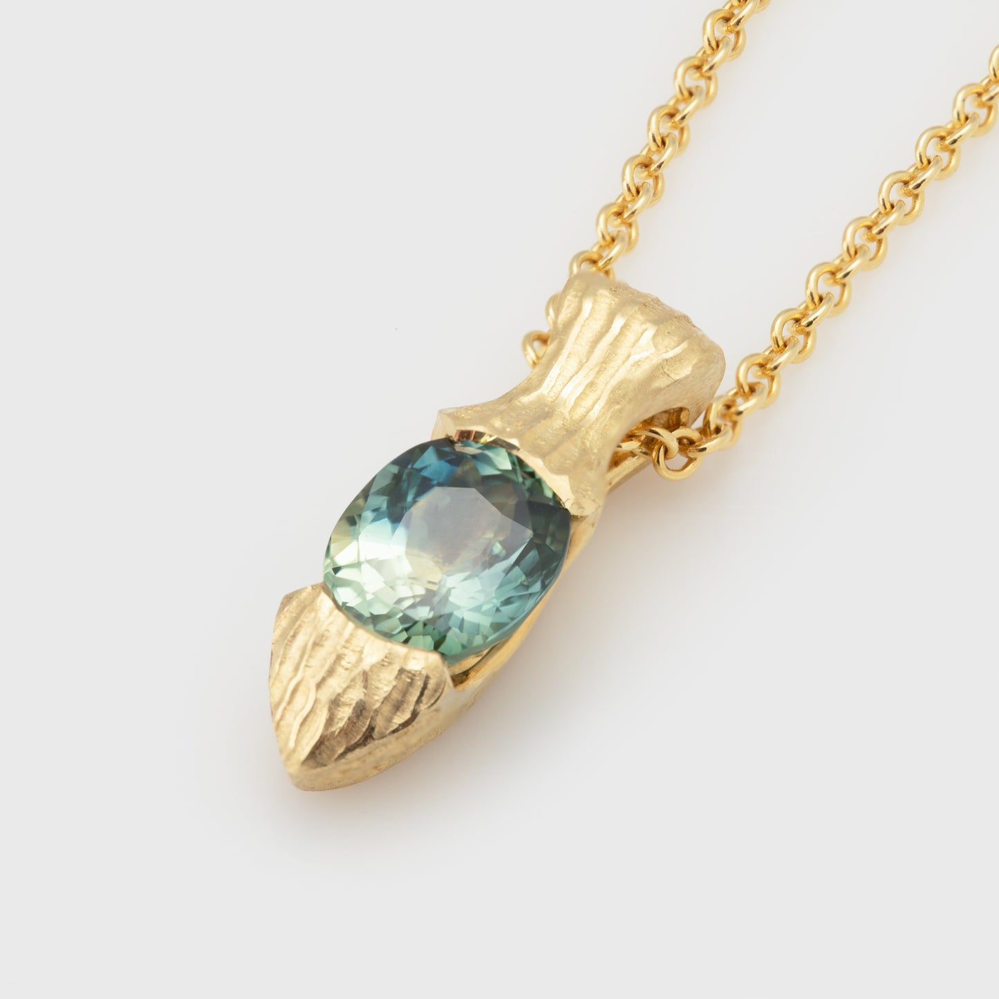 Close-up of an 18k yellow gold necklace with faceted oval green sapphire.