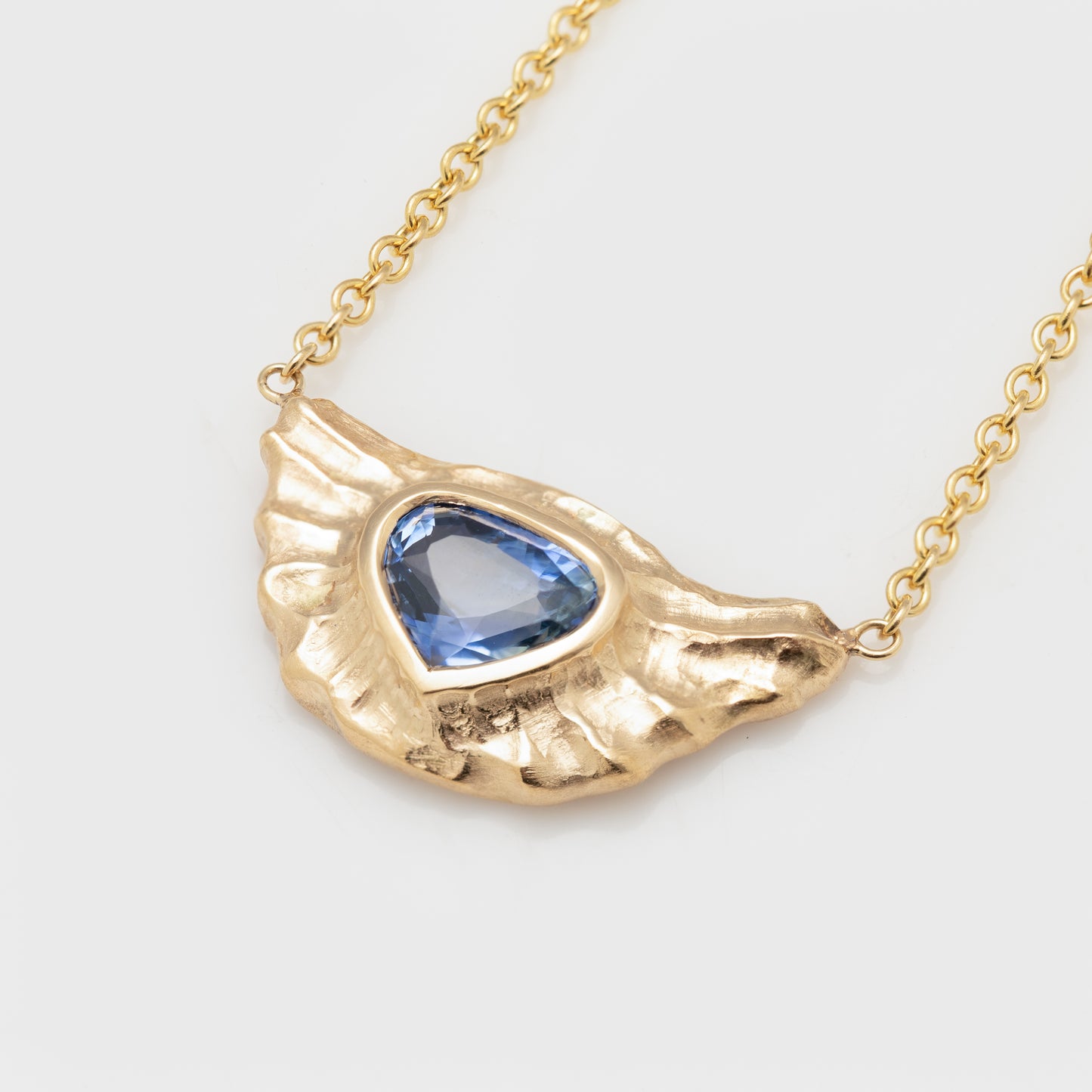Close-up of an 18k yellow gold necklace with a trillian blue sapphire.