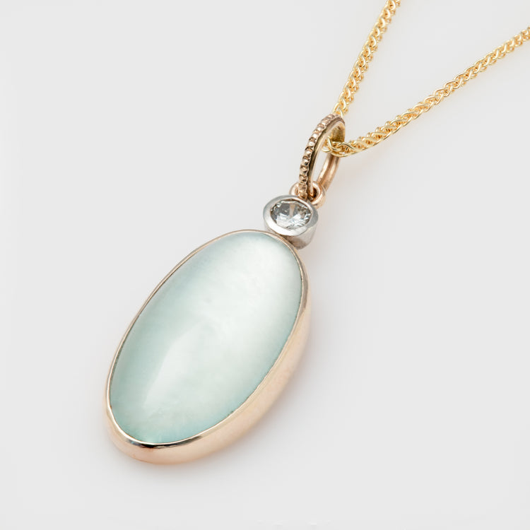 Close-up of a 14k yellow gold necklace with aquamarine and mother of pearl doublet, plus a diamond accent.