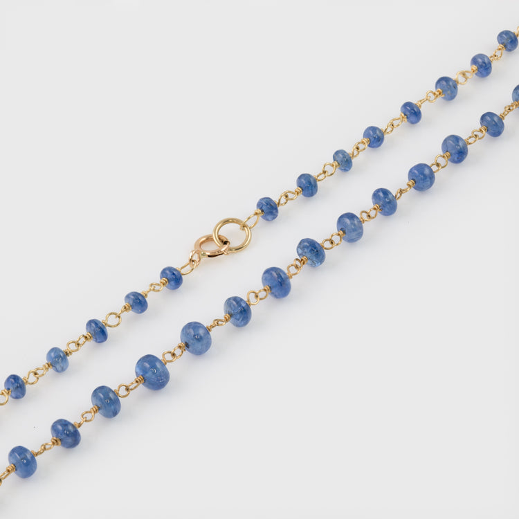 Close-up of an 18k yellow gold necklace featuring blue sapphire gemstones.