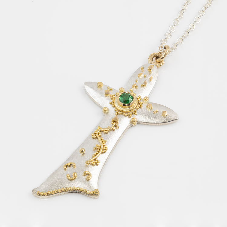 Decorative pendant with gold accents and a green gemstone on a white background