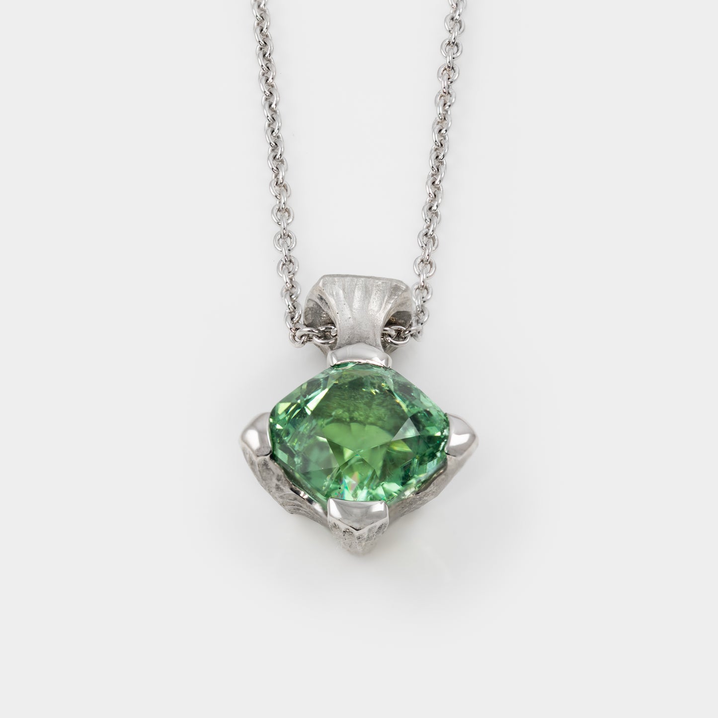 Platinum pendant with green gemstone on a white background