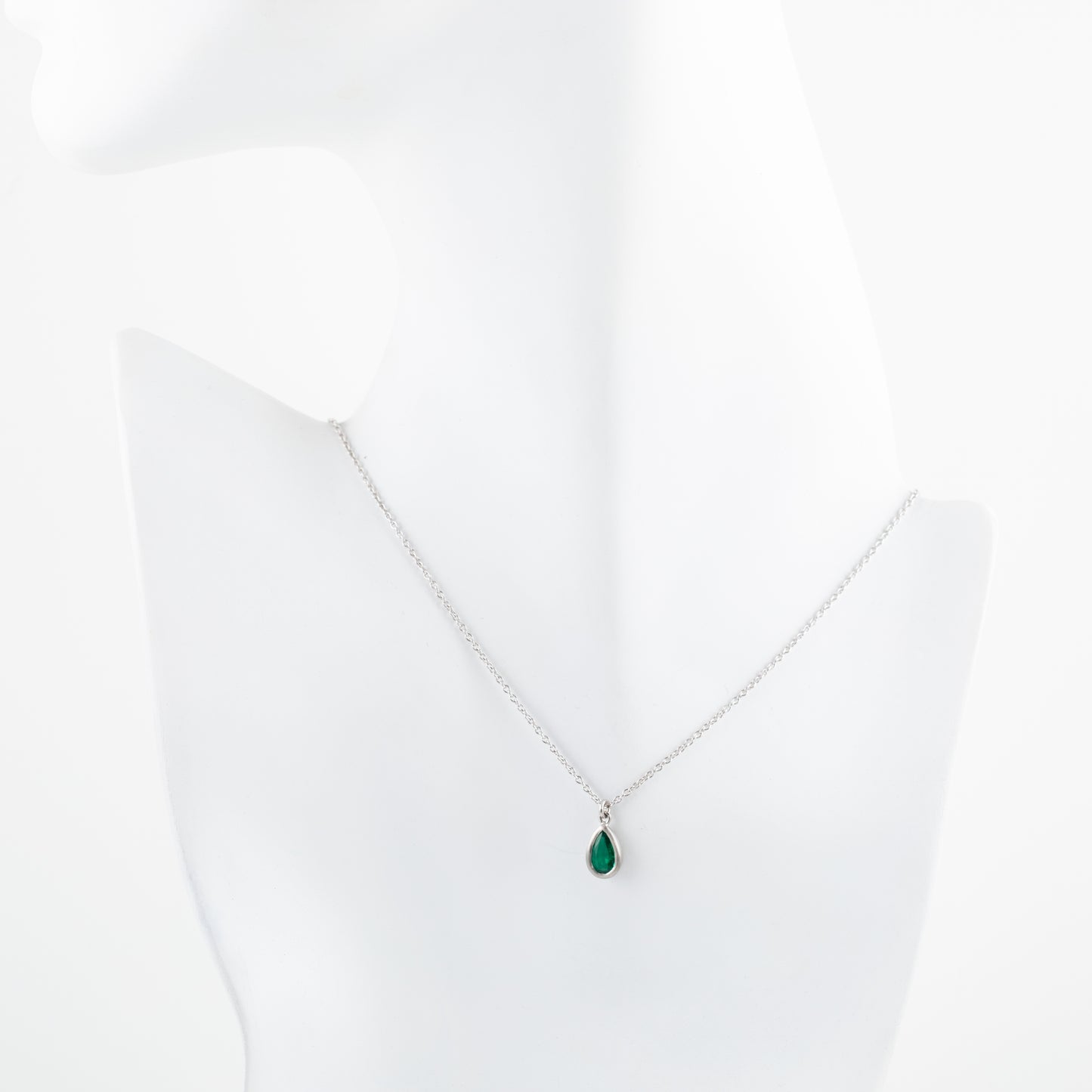 Platinum necklace with a green teardrop gem pendant on a white mannequin