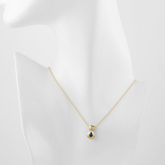 Gold pendant with a blue sapphire gemstone and an accent diamond on a white mannequin