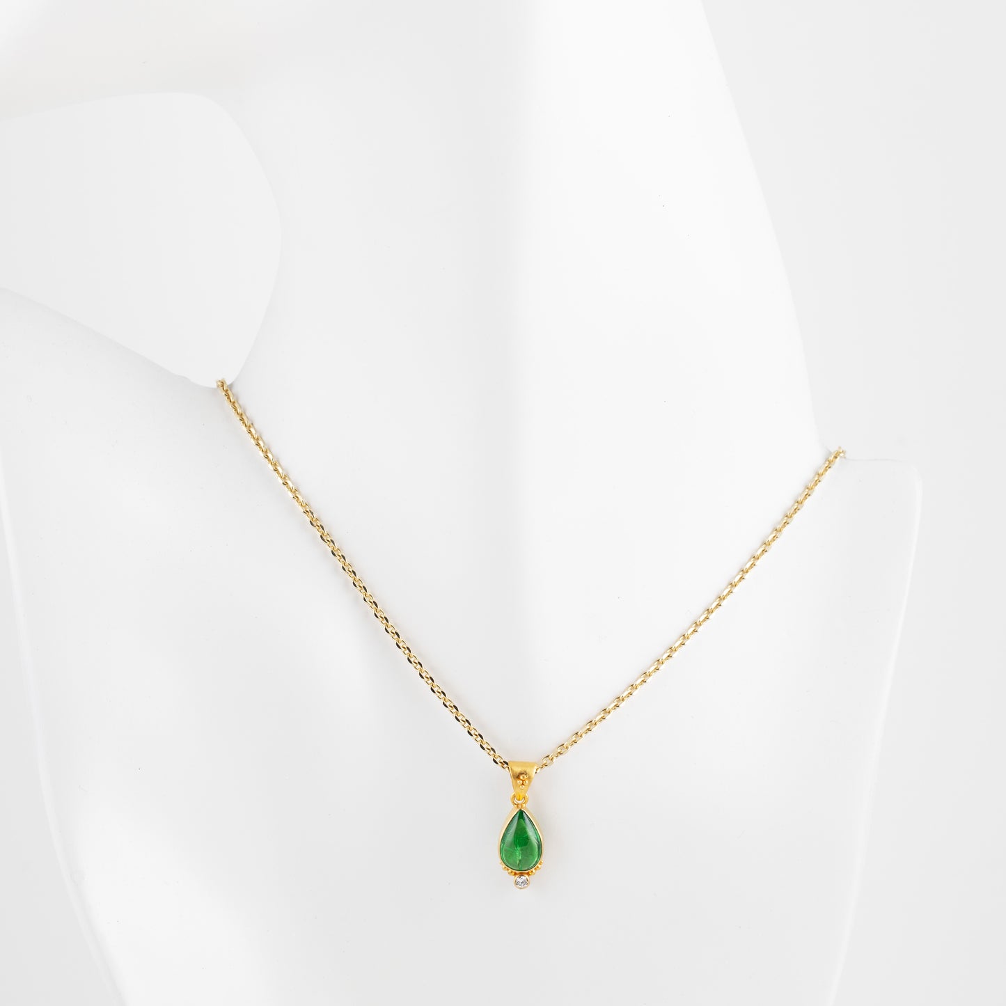 Gold necklace with a green gemstone on a white mannequin