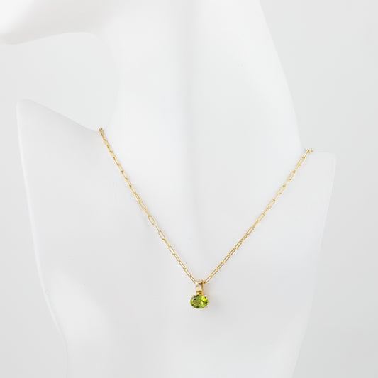 A delicate gold chain necklace with a small round green peridot gemstone pendant, displayed on a white mannequin bust against a clean white background.