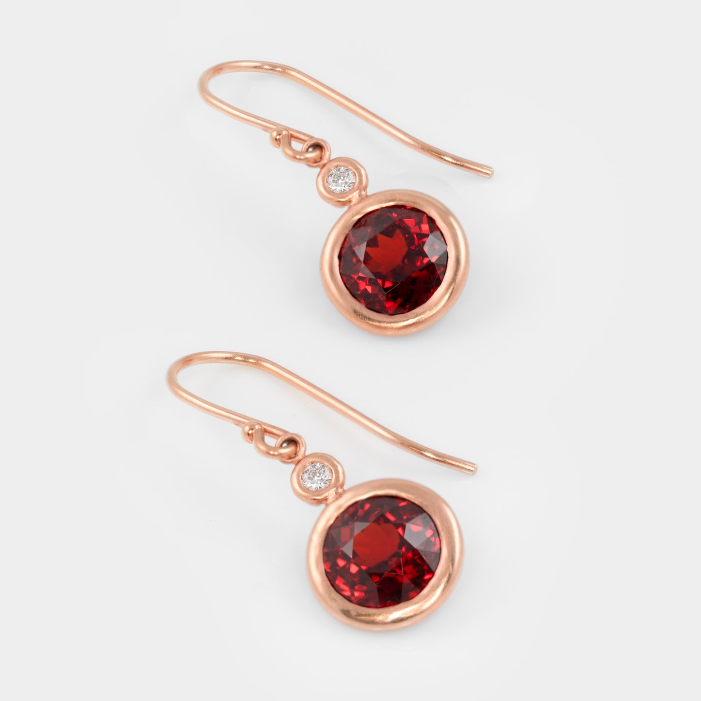 Close-up of 18k rose gold earrings with spessartite garnets and round brilliant diamonds.