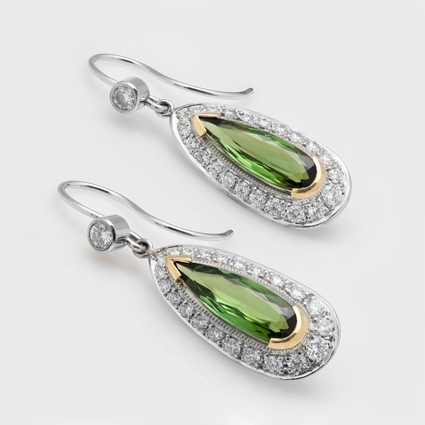 Close-up of platinum and yellow gold earrings with faceted pear-shaped green tourmaline and round brilliant cut diamonds.