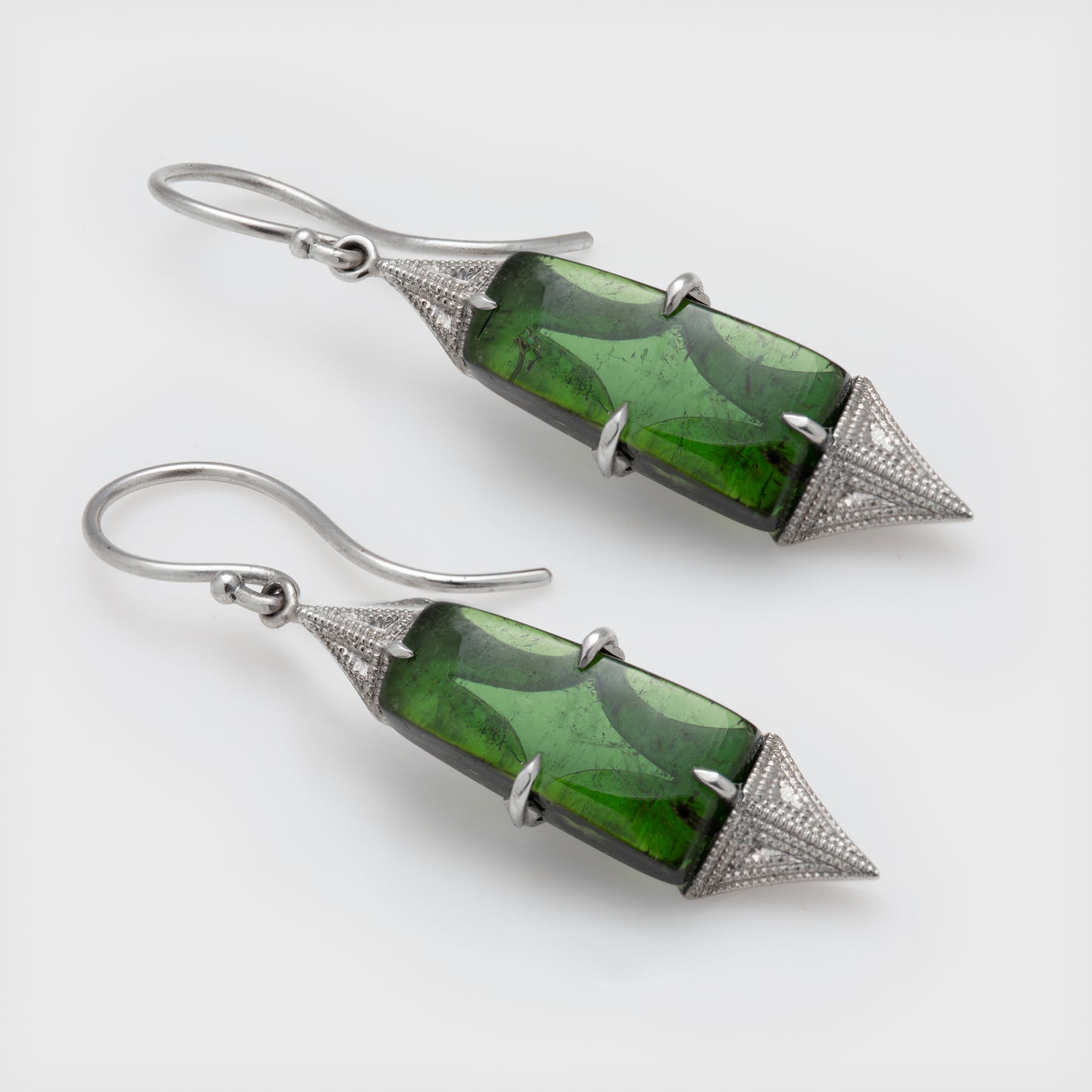 Angled view of platinum earrings with green tourmaline and milgrained metal accents.