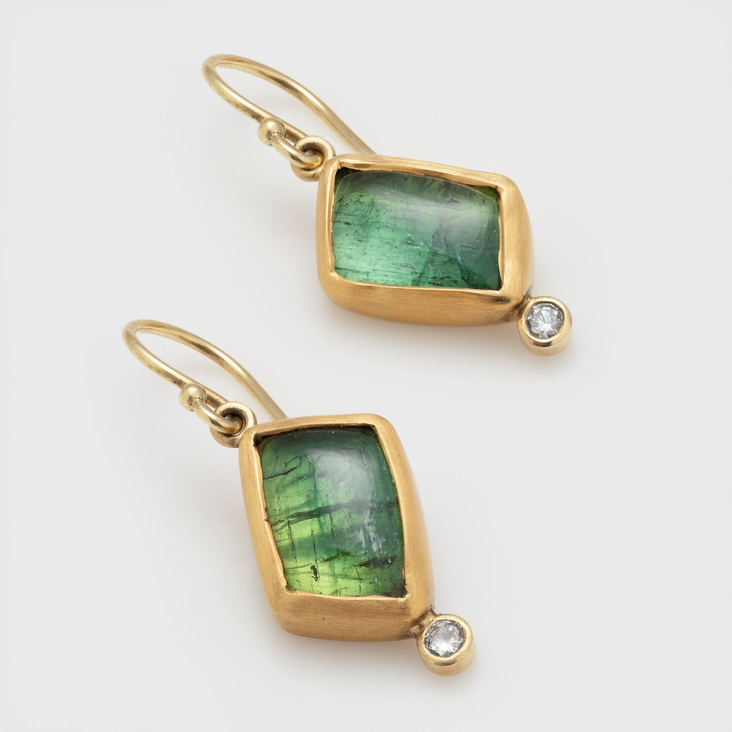 Close-up of 22k and 18k yellow gold earrings with green tourmaline and round brilliant cut diamonds.