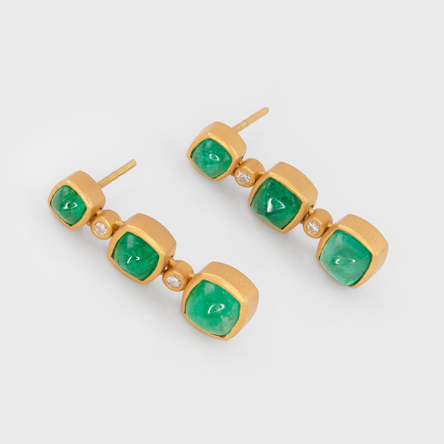Angled view of 18k matte finish yellow gold earrings with emerald cabochons and round brilliant cut diamonds.