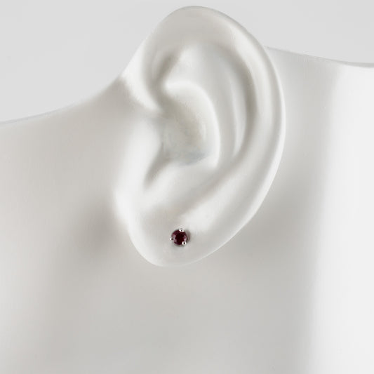 A single small stud earring with a round dark red gemstone, displayed on a white mannequin ear stand against a light gray background.