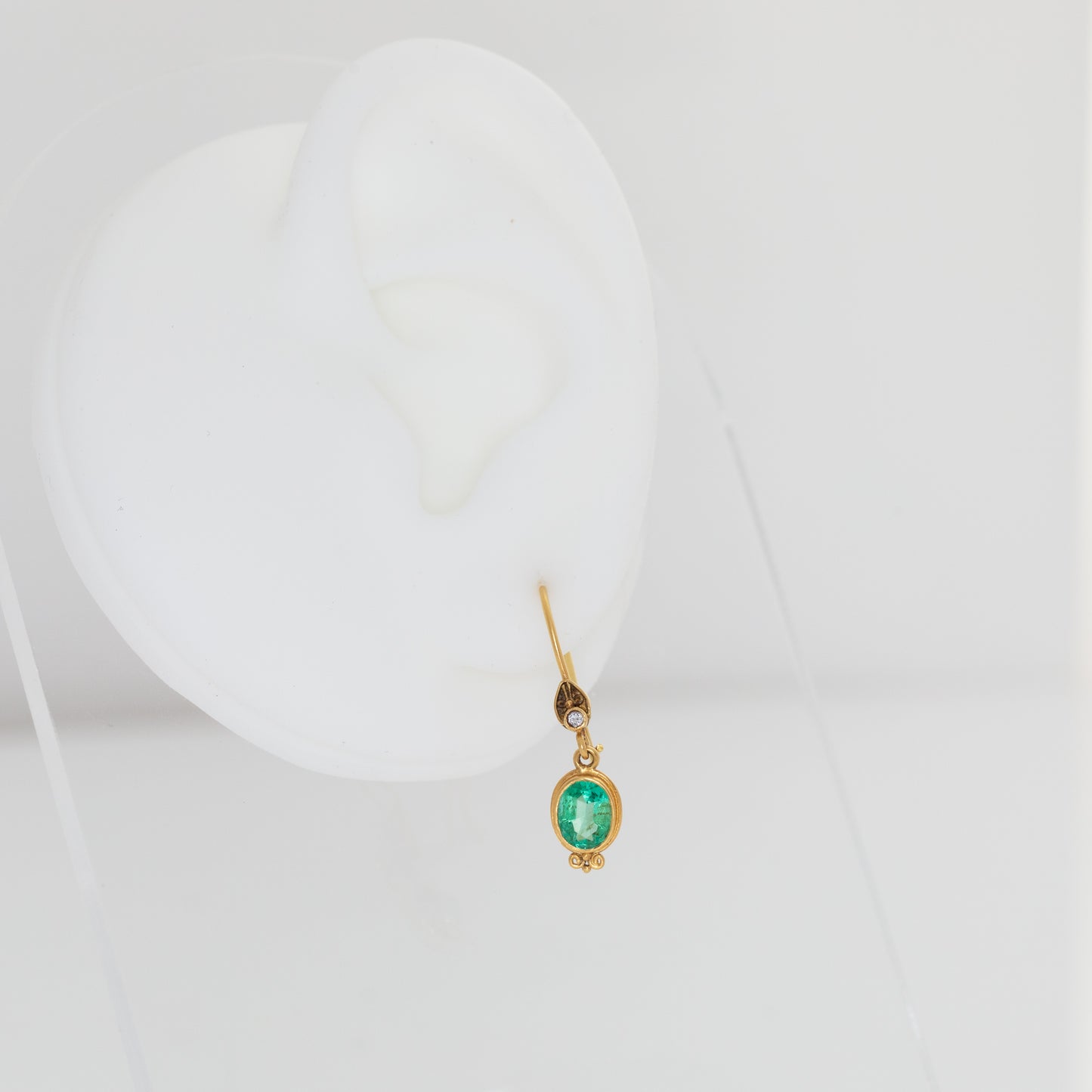 Gold earring with a green gemstone on a white background