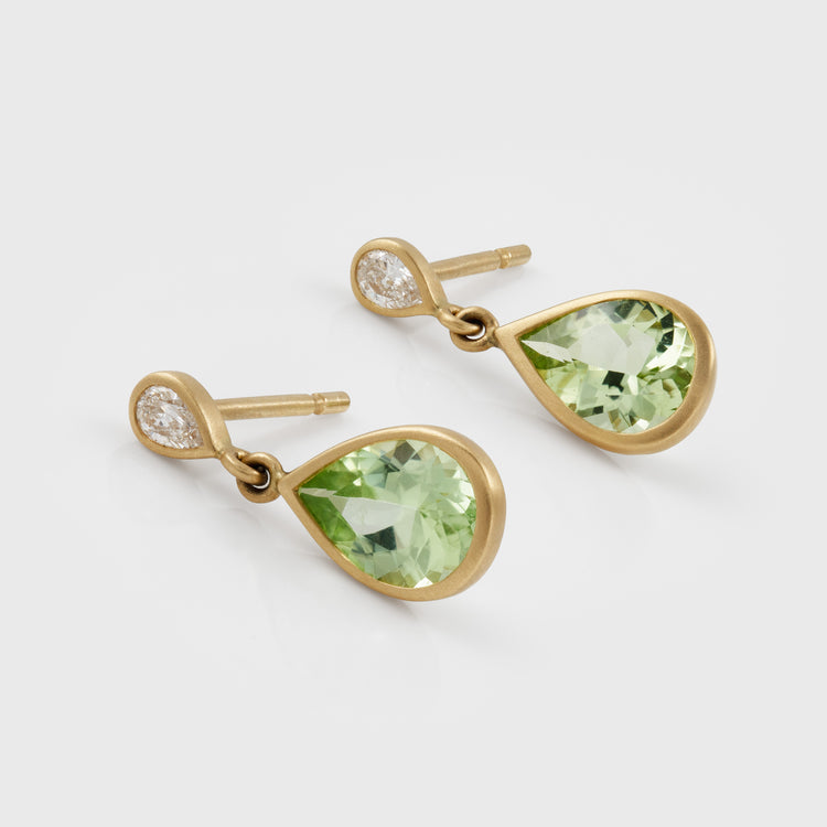 A pair of gold drop earrings featuring faceted light green teardrop-shaped gemstones and a small diamond at the top of each earring, shown on a light gray background.
