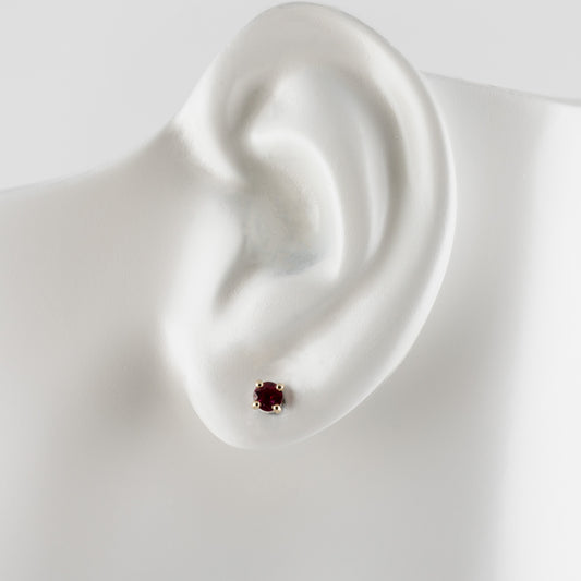 A single stud earring with a small round dark red gemstone in a gold setting, displayed on a white ear-shaped mannequin against a light gray background.