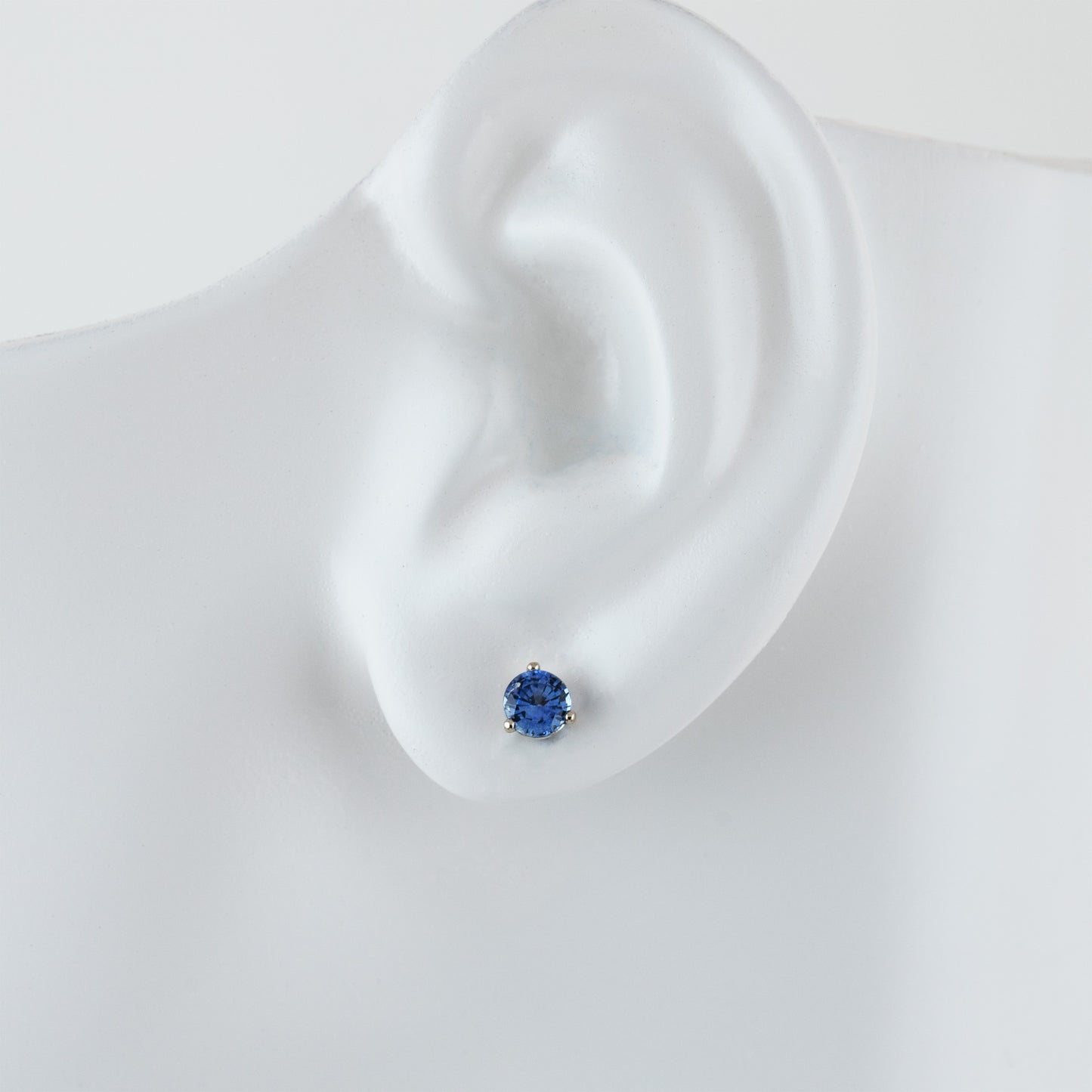 Single white gold stud earring featuring round blue Sapphire on white ear model