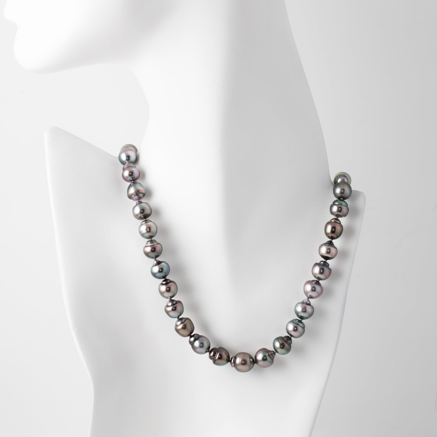 Strand of blue/purplish Tahitian pearls with a gold clasp on a white mannequin
