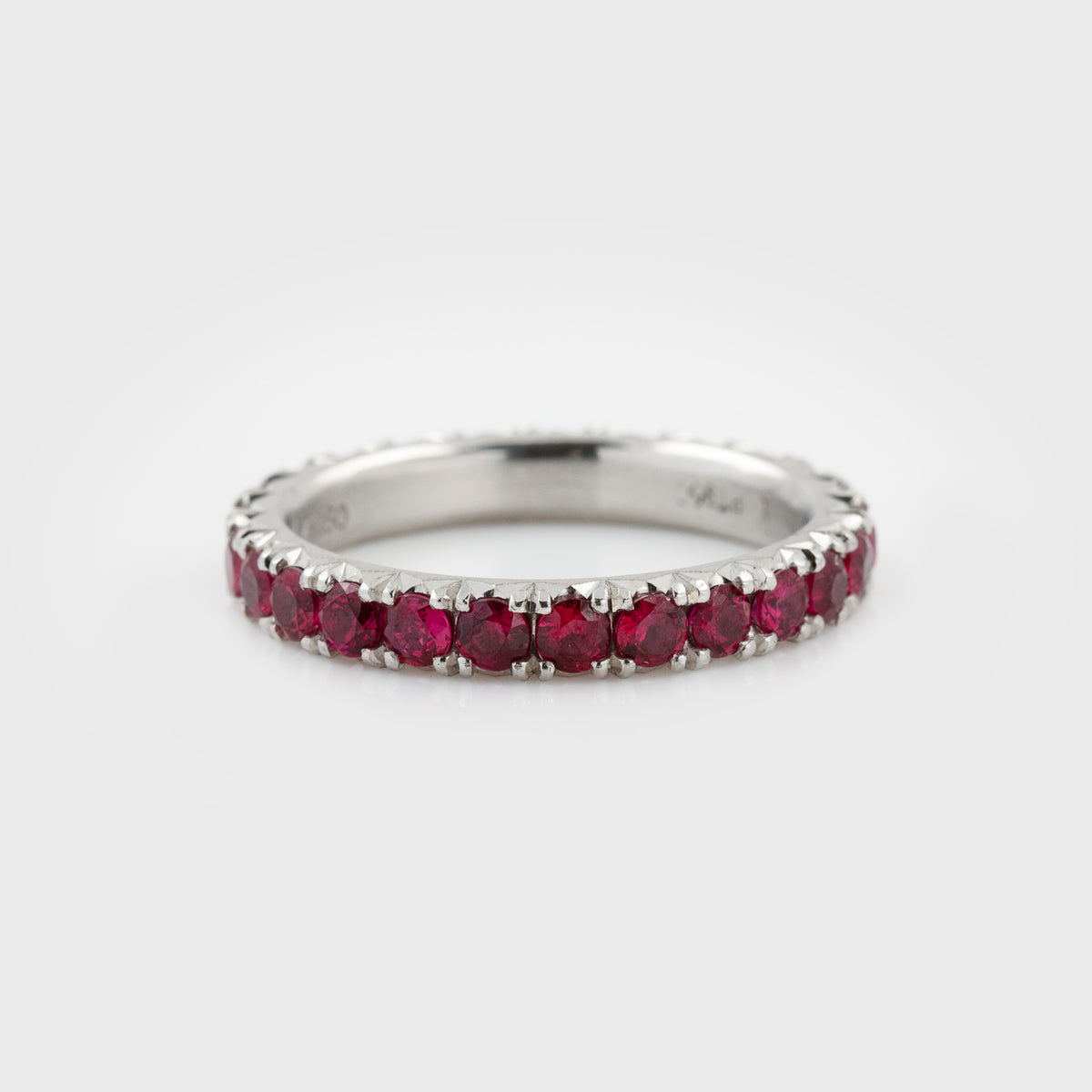 Platinum ring featuring faceted round rubies in an eternity band design with a satin finish, photographed on a white background.