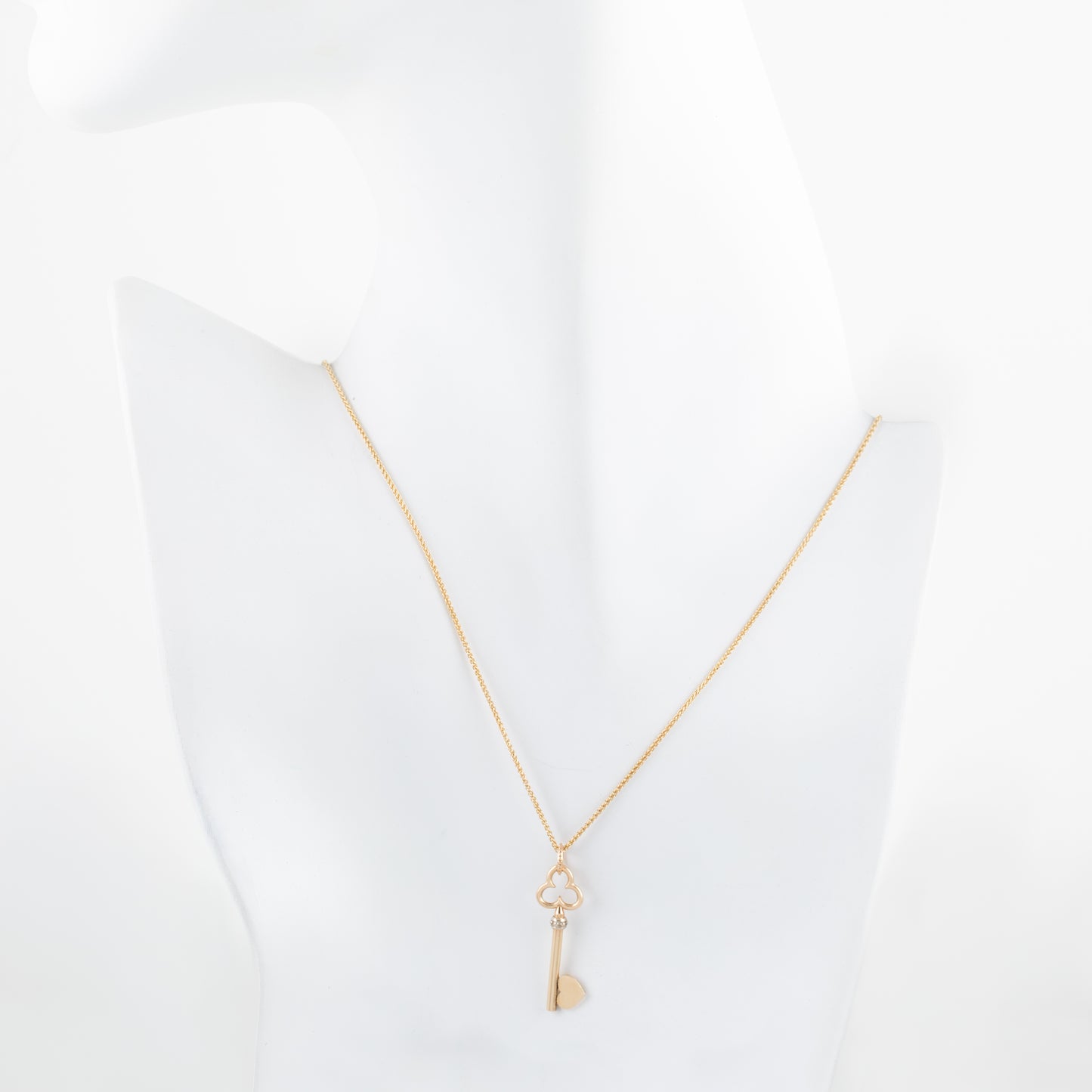 Key-shaped charm necklace on a white mannequin with a white background