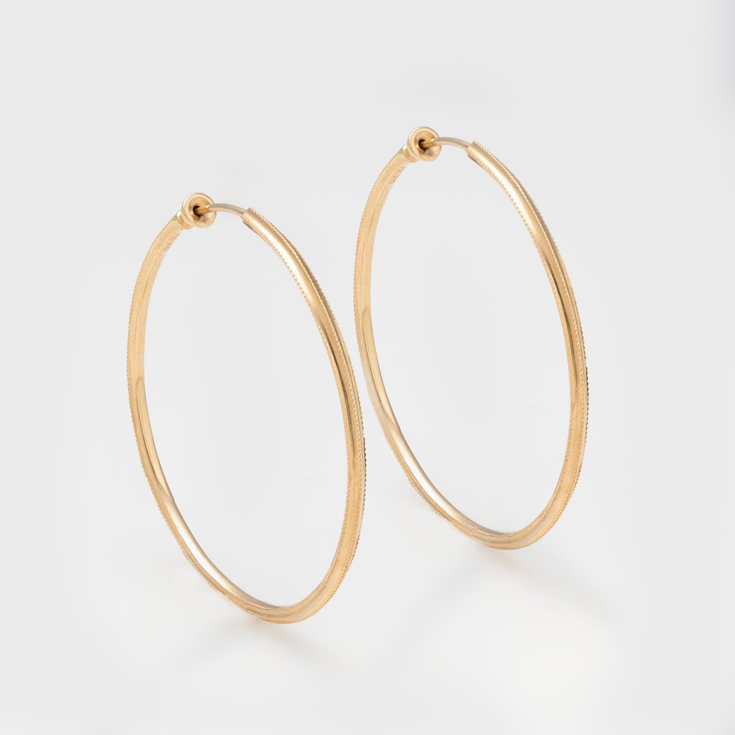 Close-up of 18k yellow gold hoops with hand-hammered texture.
